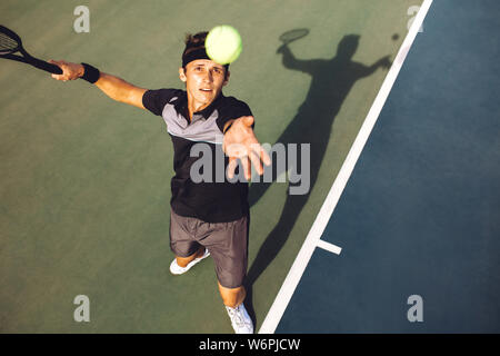 Top view of professional tennis player on baseline tossing up the ball for the serve. Young man in sportswear serving a tennis ball in a match. Stock Photo