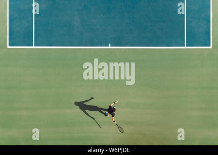 Aerial view of young male tennis player playing on hard court. Professional tennis player hitting a forehand on court. Stock Photo