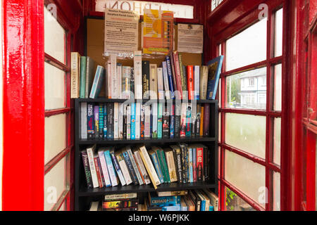 Books on shelves forming a little local library in an old red phone box / kiosk / call box in Newton Poppleford, Devon. England UK  (110) Stock Photo