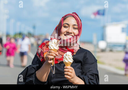 Young Asian woman eating a 99 ice cream at the seaside in Summer in the UK. Stock Photo