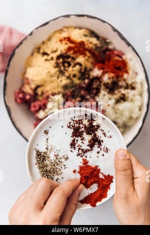 Sprinkling spices on the Turkish kofta ingredients in a ceramic bowl Stock Photo