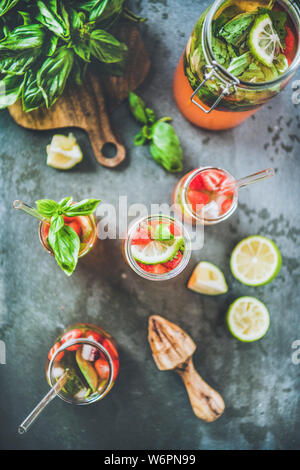 Homemade fresh strawberry and basil lemonade or ice tea in glass tumblers with eco-friendly plastic-free straws and ingredients over dark grey table b Stock Photo