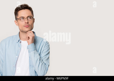 Pensive thoughtful young man pose on grey background looking aside Stock Photo