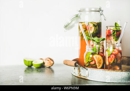 Homemade strawberry and basil lemonade or ice tea in glass tumblers with eco-friendly plastic-free straws on rustic metal tray, white wall at backgrou Stock Photo