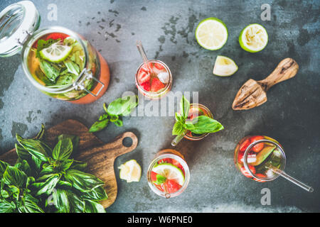 Homemade fresh strawberry and basil lemonade or iced- tea in glass tumblers with eco-friendly plastic-free straws and fresh ingredients over dark grey Stock Photo