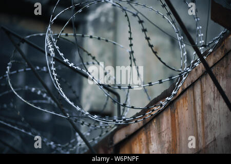 On a rusty old prison fence wound on top of a spiral metal sharp barbed wire, creating a particularly oppressive and gloomy mood Stock Photo