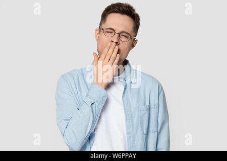 Man yawning covering mouth with hand standing on grey background Stock Photo