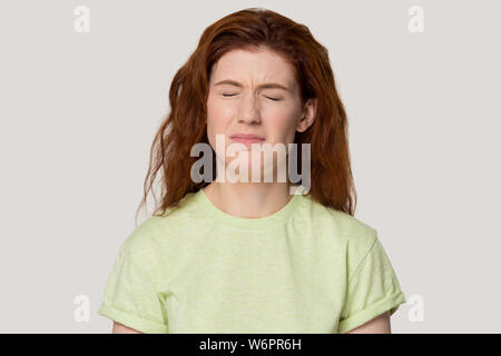 Redhead unhappy capricious woman closed eyes frowning eyebrows studio headshot Stock Photo