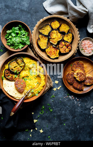 Bengali Khichdi - Lentil, Millet Soup - a Gluten-free Vegan meal served with sauteed eggplant, poppy seeds fritters, and papadum. Stock Photo