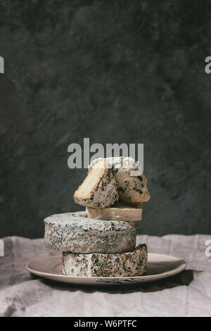 Variety of french blue cheese in stack on plate with flowing honey on grey linen table cloth. Stock Photo