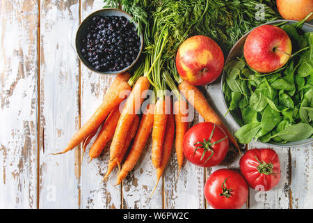 Variety of fresh fruits, vegetables and berries carrot, spinach, tomatoes, red apples, blueberries over white plank wooden background. Flat lay, space Stock Photo