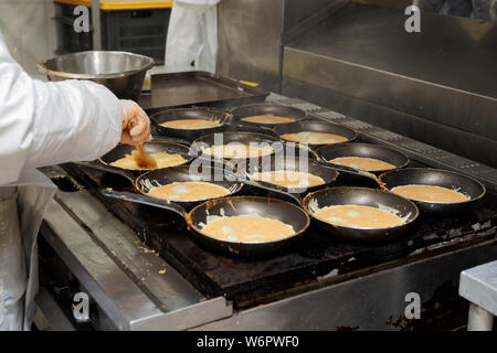 Chef is frying beaten eggs for airline meals on pans in large-scale commercial kitchen Stock Photo