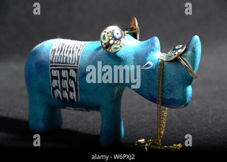 jewellery on the  little blue rhino statue hold the jewellery holder blue necklace gold rings blue and gold rings with Gray background pretty animal Stock Photo