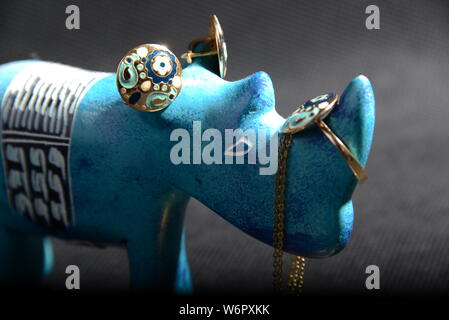 jewellery on the  little blue rhino statue hold the jewellery holder blue necklace gold rings blue and gold rings with Gray background pretty animal Stock Photo