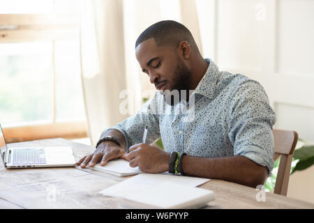 Focused african man student freelancer making notes studying with laptop Stock Photo