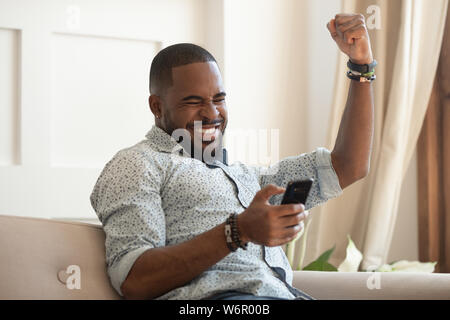 Overjoyed black man holding smartphone feeling euphoric with mobile win Stock Photo