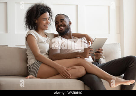 Happy young black couple using digital tablet sit on sofa