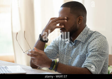 Tired african american businessman holding glasses feeling eye strain Stock Photo