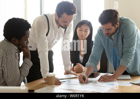 Focused multicultural team analyzing paperwork report gathered at office table Stock Photo