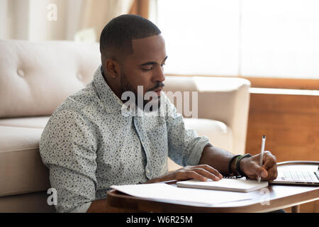 Serious african student writing notes studying at home with laptop Stock Photo