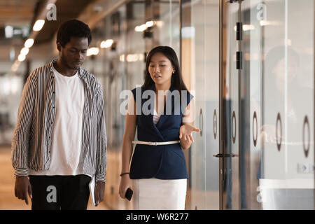 Two serious diverse colleagues talking walking in modern office hallway Stock Photo