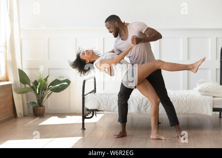 Active romantic african american couple wearing pajamas dancing in bedroom Stock Photo