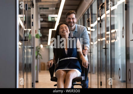 Two happy coworkers having fun ride on chair in office Stock Photo