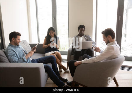 Multiethnic office workers using devices sitting in office room Stock Photo