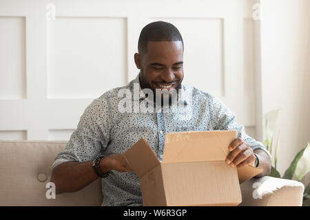 Smiling african man consumer open cardboard box get postal parcel Stock Photo