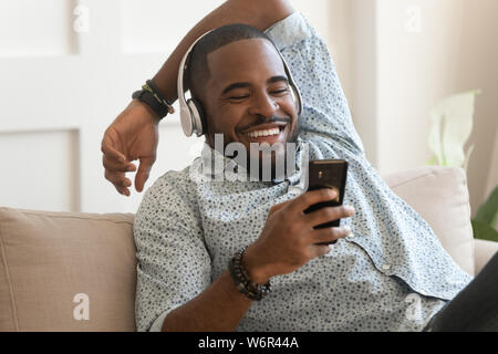 Smiling young african man wearing headphones listen to mobile music Stock Photo