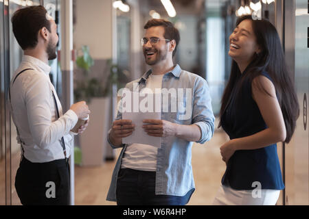 Friendly happy three diverse colleagues talking laughing at work break Stock Photo