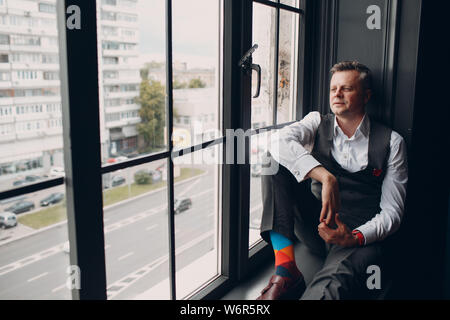 Portrait of a businessman sitting on the windowsill at big window. Business and success concept. Stock Photo