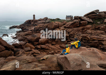 France, Brittany, Cotes d'Armor, mother and son sitting on a pink granit rock, looking at the Men Ruz lighthouse at Ploumanach Stock Photo