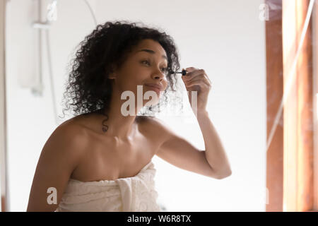 Beautiful mixed race woman looking in mirror applying mascara Stock Photo
