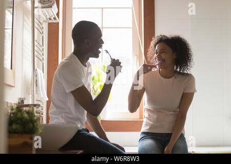 Cheerful african spouses sitting in bathroom cleaning teeth Stock Photo
