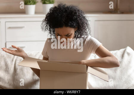 Angry african woman unpack carton box feels irritated Stock Photo