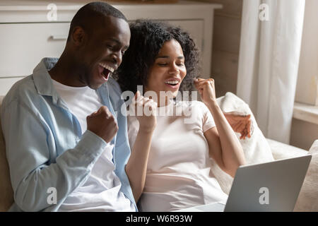 African spouses look at laptop scream with joy celebrate victory Stock Photo
