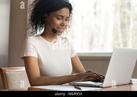 Young mixed race woman wearing headphones typing on computer Stock Photo