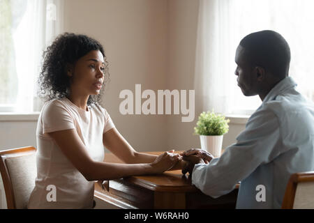 African couple sitting at table having heart-to-heart talk Stock Photo