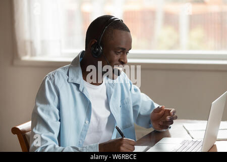 African guy wear headset making notes studying online using computer Stock Photo