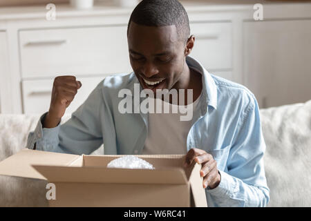 African guy looking inside carton box pleased with received parcel Stock Photo