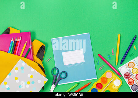 Back to school concept. Yellow backpack with school supplies and notebook on green background Stock Photo