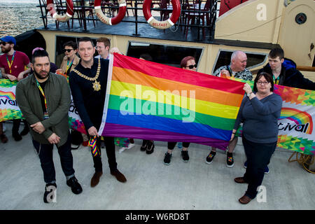 (left and right) Chair of Belfast Pride Sean O Neill and Sinn Fin's Mary Ellen Campbell present to Belfast Lord Mayor John Finucane with the first Pride flag that will fly from City Hall, following a flotilla of boats bringing Rainbow flags ahead of the Belfast Pride parade on Saturday. Stock Photo