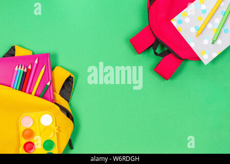 Back to school concept. Yellow and pink backpacks with school supplies, books and notebooks on light green background Stock Photo