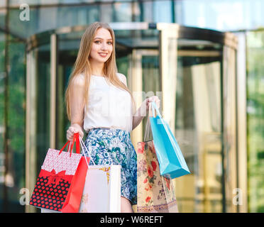 Lifestyle portrait young blonde girl, with shopping bags walking out from shop Stock Photo