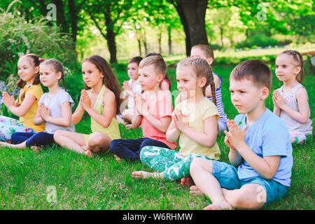 A large group of children engaged in yoga in the Park sitting on the grass Stock Photo