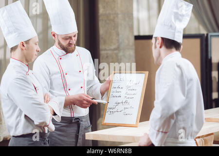 Head Chef and his staff in kitchen. interacting to in commercial kitchen Stock Photo