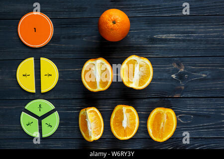 Сolorful math fractions and oranges as a sample on dark wooden background or table. Interesting creative funny math for kids. Education