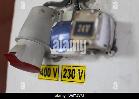 Worn out 400v, 230v and 24 industrial and multiphase power plugs and sockets on a dirty wall inside a workshop Stock Photo