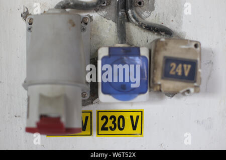Worn out 400v, 230v and 24 industrial and multiphase power plugs and sockets on a dirty wall inside a workshop Stock Photo